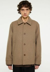 Brun ullkappa med rund krage, framknappstängning och sidofickor. Mjuk textur med avslappnad passform och minimal design.