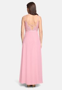 Robe longue rose avec un corsage en dentelle ajusté et des bretelles spaghetti, présentant un dos décolleté avec des bretelles croisées. Texture de jupe fluide.