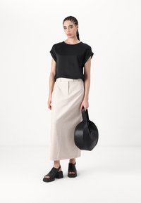 Černý top s krátkým rukávem, béžová sukně s vysokým pasem, robustní černé sandály, kulatá černá taška, minimalistický design, hladké textury, neutrální barvy.