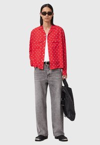 Rød skjorte med polka prikker, to brystlommer og krave, kombineret med grå bredbenede jeans og sorte accessories. Glat tekstur, afslappet pasform.