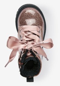 Dziecięcy błyszczący bucik w kolorze różowego złota z grubą czarną podeszwą, satynowymi sznurowadłami, bocznym zamkiem błyskawicznym i czarnym futerkiem, widoczny z góry.