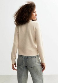 Pull en mailles beige avec des manches longues et un col rond, associé à un jean en denim délavé clair avec poches arrière.