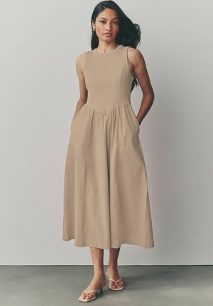 Robe sans manches beige avec un corsage ajusté et une jupe évasée. Présente des poches latérales et une texture côtelée en haut. Tissu lisse.
