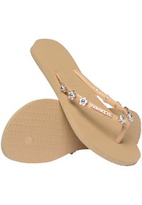 Flip-flops bej cu o talpă din cauciuc texturat. Bretele transparente decorate cu accente argintii și florale. Numele brandului afisat pe bretea.