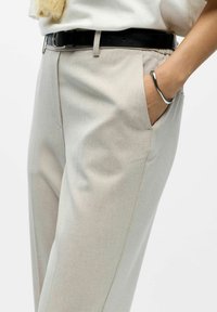 Bežne krojene hlače s glatkom teksturom, s bočnim džepovima i crnim kožnim remenom s srebrnom kopčom. Minimalistički dizajn.