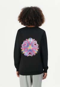 Black sweatshirt featuring a colorful, intricate circular pattern on the back. Material appears soft; design includes swirls, eyes, and floral accents.