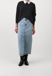 Jeans-Maxirock in Hellblau mit geradem Schnitt und sichtbarer Naht vorne. Kombiniert mit einem schwarzen Pullover und schwarzen Stiefeletten.