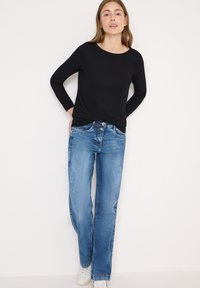 Top nero a maniche lunghe a coste abbinato a jeans dritti azzurri e sneakers bianche. Linee pulite e design minimalista senza motivi visibili.