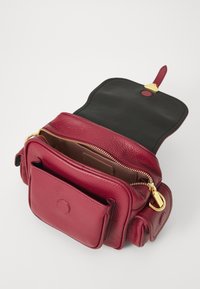 Burgundy leather handbag with a textured finish, featuring a main zip compartment, front pocket, and gold hardware accents. Open design.