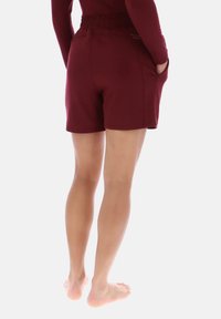 Bordeauxrode sportshorts met een elastische tailleband, zijzakken en een gladde textuur, gezien van achteren. Zachte, aansluitende pasvorm duidelijk zichtbaar.