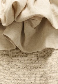Platnena tkanina u bež boji s teksturiranim, nabranim gornjim dijelom i smokanom donjom sekcijom, s ravnomjerno raspoređenim elastičnim šavovima.