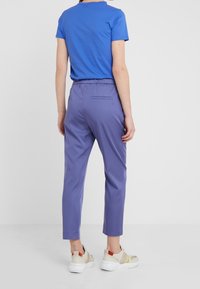 Niebieska koszulka z krótkim rękawem noszona z fioletowymi dopasowanymi spodniami. Spodnie mają elastyczny pas i jedną tylną kieszeń. Całość dopełniają białe trampki.