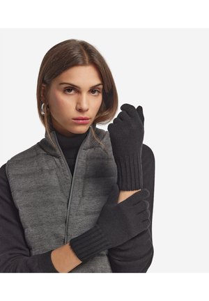 Guanti neri a coste con una texture morbida, indossati da una persona con un gilet grigio. I guanti presentano una vestibilità aderente con polsini allungati.