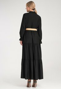 Czarna, maxi sukienka z długim rękawem z falbanistym dołem, ze ściągniętą talią podkreśloną plecionym paskiem, gładka tekstura i prosty design.