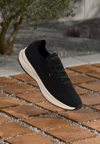 Black knit sneakers with a textured surface, cream midsole, and black outsole. Features dark laces and a logo on the tongue.