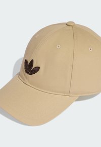 Béžová látková baseballová čepice s prohnutým kšiltem. Na přední straně je tmavě hnědé vyšívané logo a větrací průduchy.