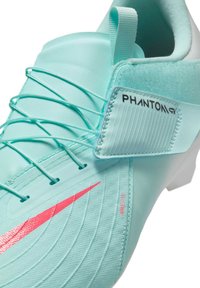 Világoskék focicipő texturált szintetikus anyagból, rózsaszín Nike logóval, állítható fűzőrendszerrel és párnázott bokaléccel.