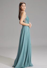 Turkoosi iltamekko, jossa on kimalteleva vartalo, ohuet hihnat ja virtaava hame; pehmeäteksturoitu kangas, jossa on kiiltävä pinta.