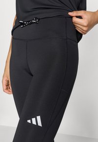 Leggings deportivos negros con una pretina alta, con acabado texturizado y detalle de logo blanco. Incluyen un cordón decorativo en la cintura.