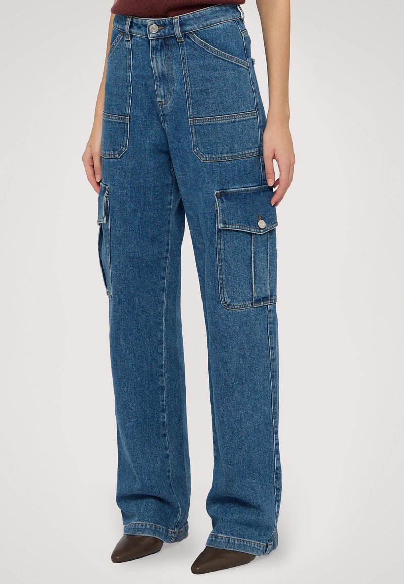 Modré denimové cargo kalhoty s uvolněným střihem, velkými bočními kapsami a vybledlou texturou. Obsahují poutka na opasek a přední zapínání na knoflík.