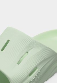 Κοντινό πλάνο ανοιχτού γκριζοπράσινου σανδαλιού με υφή στην επιφάνεια και οπές αερισμού στο πάνω μέρος.