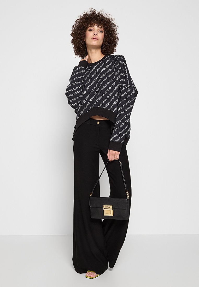 Suéter negro de gran tamaño con estampado de texto blanco, combinado con pantalones amplios de tiro alto negros y un bolso negro con detalles dorados.