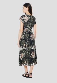 Robe midi fleurie noire et verte avec des accents roses, manches courtes, taille élastique et jupe fluide. Associée à des sandales noires à brides.