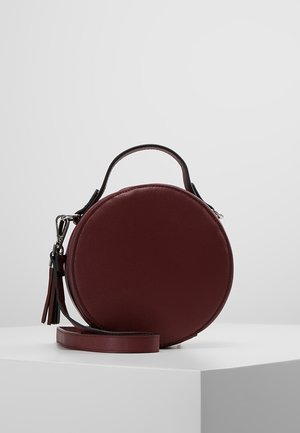 Rund burgunderfarvet taske med en tekstureret overflade, et hanke øverst og en aftagelig skulderrem; har et frynseaccent og sølvfarvet hardware.
