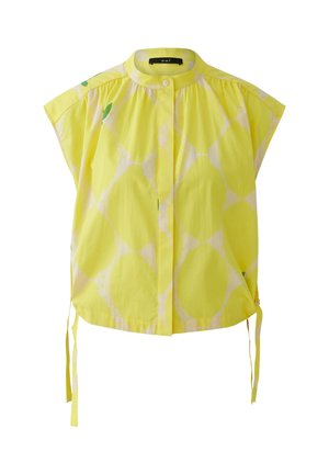 Geel kortärmelig bloesje met subtiel wit cirkelpatroon, mandarijnkraag, knoopsluiting en zijstrikjes aan de zoom.