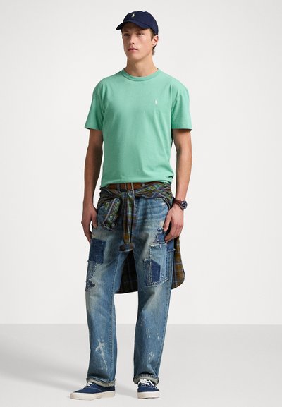 Mintgrön t-shirt med rund hals, slitna denimjeans med lappar, rutig skjorta knuten i midjan, marinblå keps och blå sneakers.