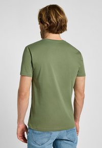 Oliwkowa bawełniana koszulka z okrągłym dekoltem i krótkimi rękawami, gładka tekstura, w połączeniu z jasnoniebieskimi dżinsami. Minimalistyczny design.