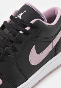 Černé kožené tenisky s růžovými detaily, bílou podrážkou, zaoblenou špičkou a černými tkaničkami. Na jazyku je viditelné logo Jumpman.