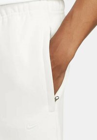 Weiße Sportshorts mit einer Seitentasche, ausgestattet mit einem kleinen, runden Reißverschluss. Ein dezentes Nike-Logo ist auf dem Stoff sichtbar.