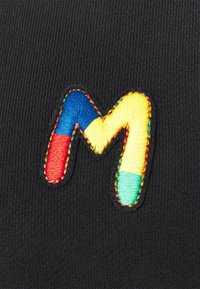 Letra "M" bordada en multicolor, en azul, rojo, amarillo y verde, sobre tejido de canalé negro.