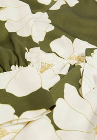 Tessuto con motivo floreale che presenta grandi fiori bianchi su uno sfondo verde scuro, con una superficie liscia e bordi di tessuto arricciati.