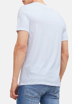 Uomo che indossa una semplice t-shirt bianca a maniche corte e jeans di jeans blu, mostrato di spalle su uno sfondo bianco.