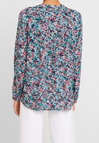 Blusa floreale con sfondo blu navy e piccoli fiori multicolori. Maniche lunghe, scollatura rotonda e vestibilità comoda.