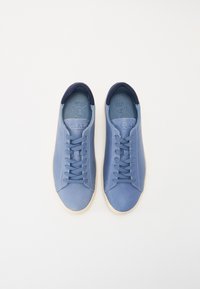 Blue sneakers with a smooth texture, featuring a darker blue collar, flat laces, and a light beige rubber sole. CLAE branding visible inside.