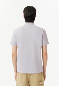 Polo de manga corta en gris claro, con un cuello clásico y textura suave. Sin patrones ni acentos visibles. Diseño simple y limpio.