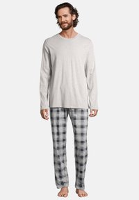 Chemise à manches longues gris associée à un pantalon de pyjama à carreaux blanc, marine et gris. Texture de tissu douce avec une coupe décontractée.