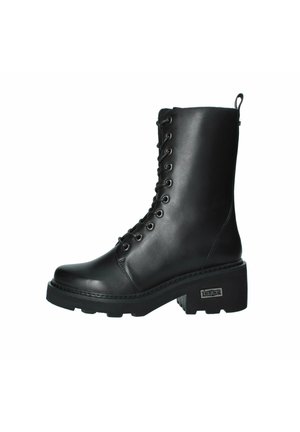 Stivale alla caviglia in pelle nera con lacci, dotato di un tacco chunky, punta rotonda e suola in gomma resistente. Presenta occhielli metallici e un tassello per il tiraggio.