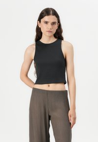 Must mustretniku mustretnik ja ringikäärlates ja ribatatud tekstuuriga must cropped tank top, millele on püstitatud kõrge vöökoht ja volditud pruunid püksid.