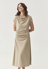 Abito beige con collo a cowl, corpino drappeggiato, maniche a cappuccio e dettagli arricciati in vita e gonna. Tessuto liscio e leggero.