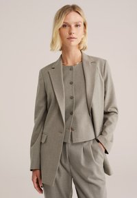 Hallide hall blazer, kusete lõikega krae, esikottide ja siledast tekstuurist. Kanna sellele sobivat nööpidega pluusi. Minimalistlik disain.