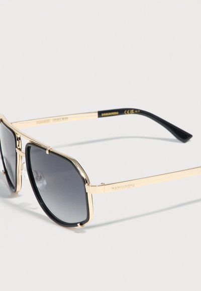 Γυαλιά ηλίου με χρυστό μεταλλικό σκελετό, μαύρους τετραγωνισμένους φακούς με βαθμιαία σκίαση και μαύρες άκρες στα μπροστινά σκέλη σε λευκό φόντο.