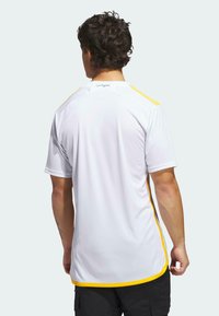 Vit idrottströja med korta ärmar, med gula ränder längs axlarna. Slät textur, något svängd fåll. "Los Angeles" tryckt på kragen.