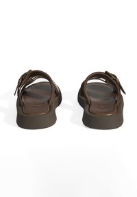 Sandales brunes au design minimaliste, dotées d'une semelle plate, de sangles réglables et d'une texture en cuir lisse. Accent en métal doré.