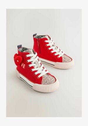 Baskets montantes rouges avec un devant pailleté, des lacets blancs, une semelle en caoutchouc texturée et un pendentif en forme de cœur avec un visage souriant.