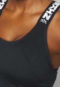 Débardeur de sport noir à larges bretelles avec accents de logo blanc. Tissu lisse et léger avec de petites perforations pour la respirabilité.