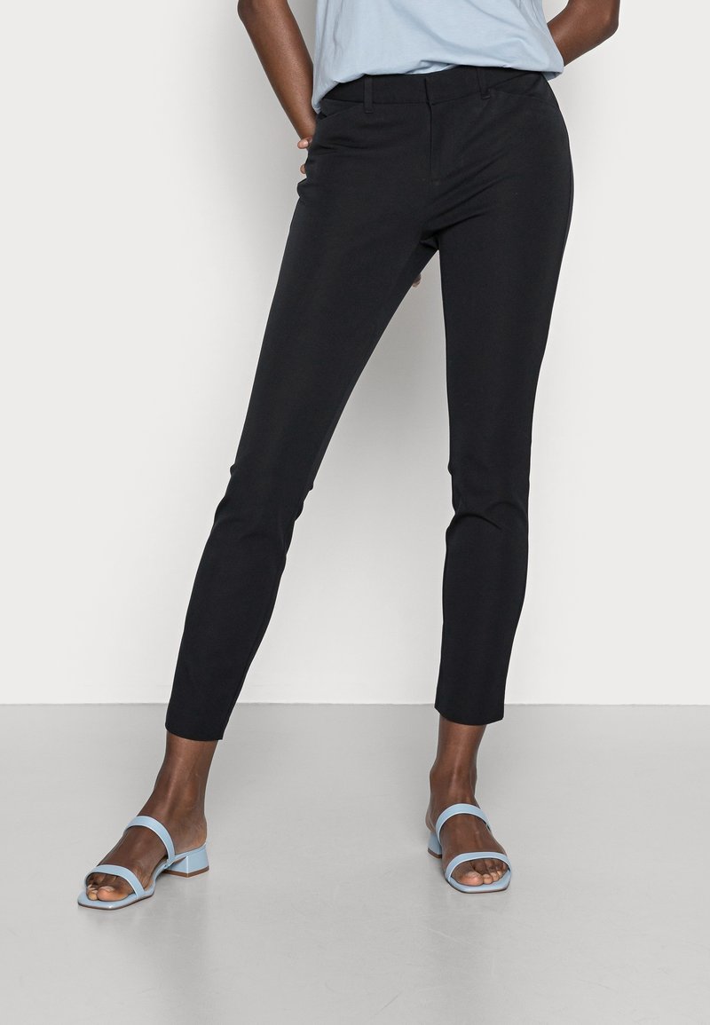 Pantalon noir slim à la texture lisse et au design sur mesure, doté de poches standard et d'une taille mi-haute. Associé à des sandales bleu clair.
